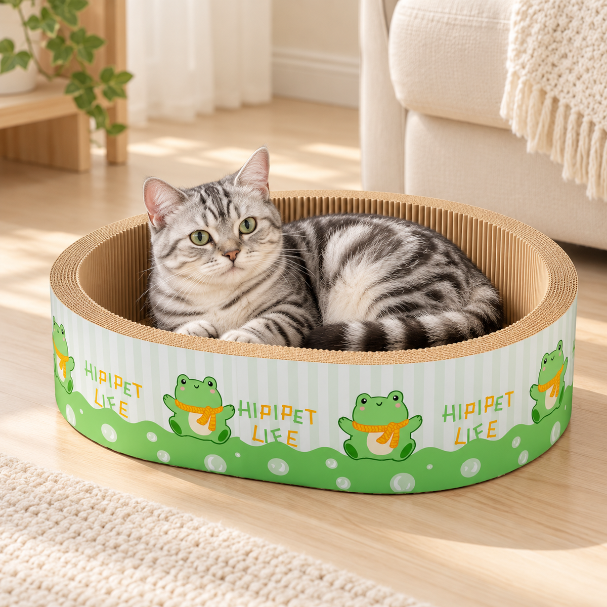 Silver tabby cat resting inside an oval cardboard cat scratcher bed with a green frog design